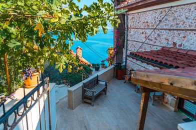 Sonnige Terrasse mit Bänken und Pflanzenkübeln, die über ein ruhiges blaues Meer blickt, i